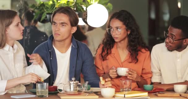 Beskär syn på glada multietniska kollegor kommunicera och dela idéer medan du äter i mysiga café. Millennial startupers prata och njuta av fritid. Begreppet livsstil. — Stockvideo
