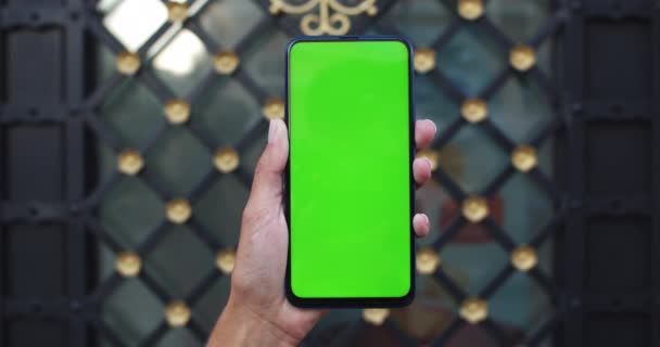 Detailní pohled na ženskou ruku držící smartphone s makupem šablony obrazovky. Koncept zeleného plátna a chromatického klíče. Stylové kovové a skleněné dveře na pozadí. — Stock video