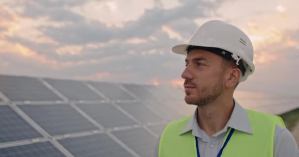 Vista delle colture di ingegnere maschio caucasico in uniforme. Uomo barbuto in casco protettivo a piedi presso la centrale solare per l'esame. Concetto di sviluppo delle centrali solari e di energia verde. — Video Stock