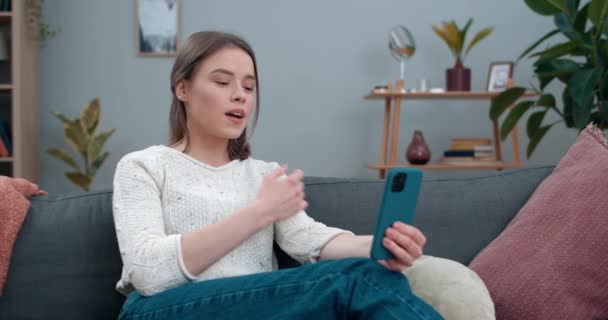 Mooie vrouw tonen met doofstomme gebarentaal zin Ik mis je tijdens het zitten op sofa.Millennial vrouwelijke persoon met behulp van smartphone tijdens het hebben van videogesprek. Gehoorverlies. — Stockvideo