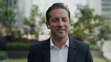 Kulaklıklı neşeli iş adamının portresi ve kamera görüntülerindeki ortakları dinliyor. Gülümseyen olgun yönetim, sokaktaki çevrimiçi toplantıda müşteriye danışıyor