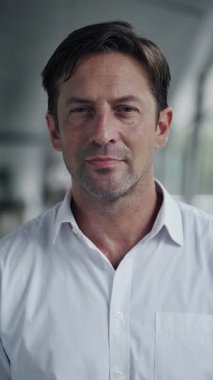 Tişörtlü kendine güvenen işadamının portresi, ticari binanın dikey çekim lobisinde kameraya doğru dönüyor. Başarılı bir esmer şirket lideri ofiste profesyonellik yayıyor.