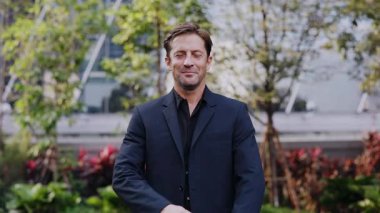 Kendine güvenen iş adamının portresi modern şehir bahçesinde gülümsüyor ve kollarını kavuşturuyor. Şirketin CEO 'su şehir merkezindeki parkta profesyonellik ve başarı yayıyor.