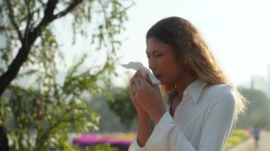 Hasta Asyalı kadın portresi burnu akıyor ve yeşil bahar parkında duruyor. Beyaz gömlekli üzgün kadın hapşırıyor yeşil şehir bahçesinde yürüyen alerji belirtilerinden muzdarip.