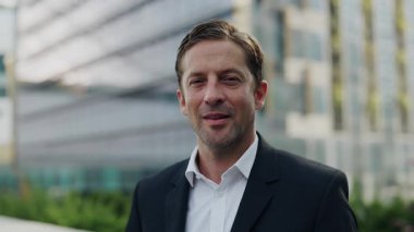 Şehir merkezindeki kameraya bakan başarılı iş adamının portresi. Şirket başarılarından gurur duyan olgun şirket CEO 'su ofis binasının önünde duruyor.