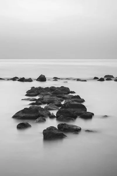 Siyah ve beyaz güzel sanatlar fotoğraf Beach'te. Rock ve dalga deniz hareket ile hareketli arka plan gökyüzü
