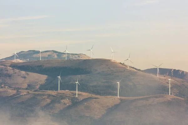 Global warming, climate change. Turbines on the field on the sunset sky. Alternative energy source. Wind farm in Italy. Eco power, green technology concept.