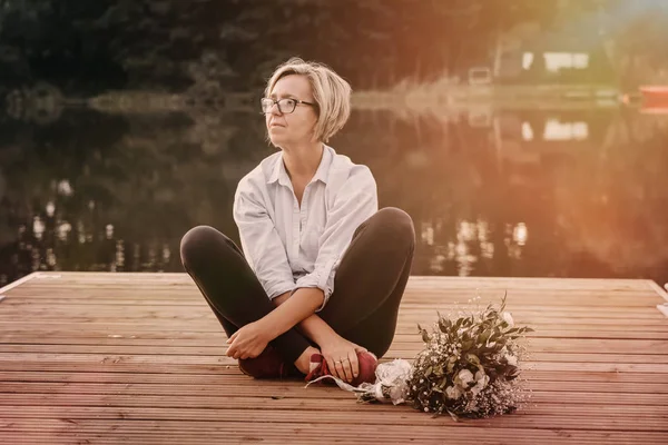 Demet çiçek kopya alanı ile pier üzerine oturan üzgün yalnız güzel kadınla