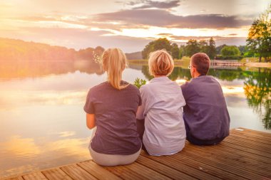 Ahşap iskele günbatımı sırasında oturan üç mutlu insanlar