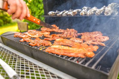 Sıcak kömürle hazırlanmış ve lezzetli dumanlı domuz pastırması pişiren küçük bir barbekü.