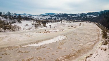 Donmuş kış nehri. Karlı köy ve yolun havadan görünüşü. Baharın başlarında eriyen kar ve buz.