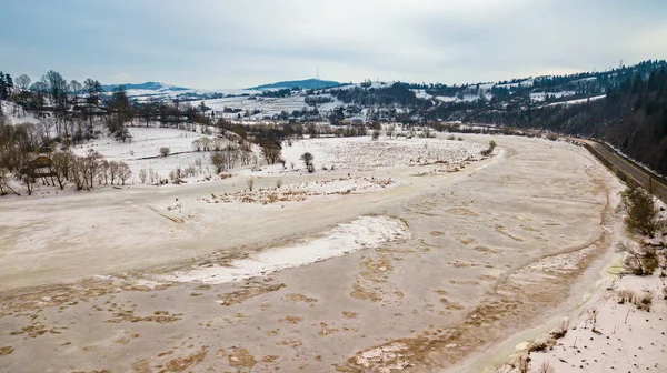 Donmuş kış nehri. Karlı köy ve yolun havadan görünüşü. Baharın başlarında eriyen kar ve buz.