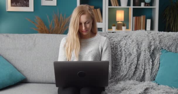 Beautiful lady sitting on couch and working on laptop — Stock Video