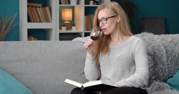 Güzel bir kadın evde kitap okurken kırmızı şarap içiyor. — Stok video