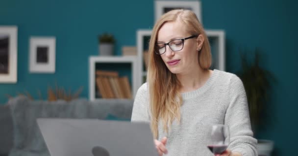 Чарівна жінка працює на ноутбуці і п'є червоне вино — стокове відео
