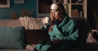 Bornozlu kadın kahve içiyor ve dizüstü bilgisayarla çalışıyor.