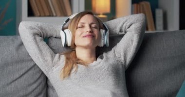 Kulaklıkla şarkı dinlerken kanepede dinlenen bir kadın.