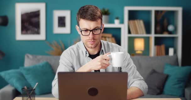 Hombre guapo usando el ordenador portátil mientras está sentado en la mesa con café — Vídeo de stock