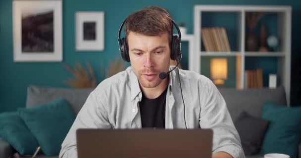 Confident man in headset having video chat on laptop at home — Stockvideo