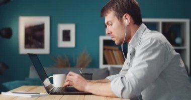 Side view of man in earphones working on laptop