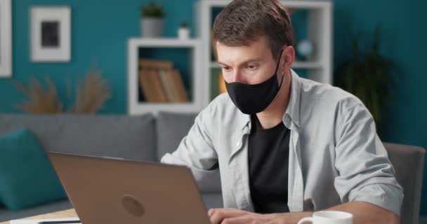 Responsible man in medical mask working on laptop at home — Stock video