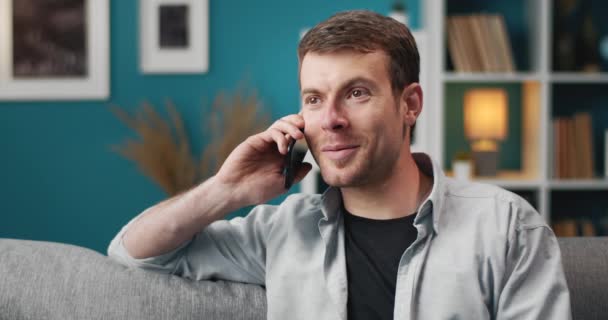 Happy bearded man talking on phone while relaxing on couch — 图库视频影像