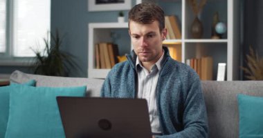 Concentrated man sitting on couch and working on laptop