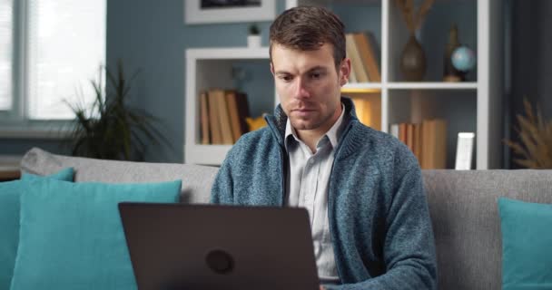 Homem concentrado sentado no sofá e trabalhando no laptop — Vídeo de Stock
