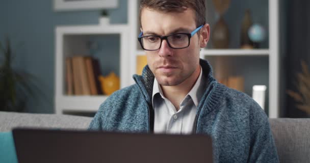 Confident man sitting on couch and working on laptop — Αρχείο Βίντεο