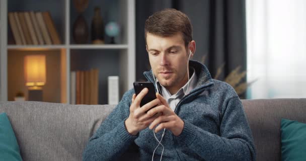 Young man in earphones listening music on smartphone — Stockvideo