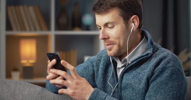 Cheerful man in headphones enjoying favorite songs on phone — Stockvideo