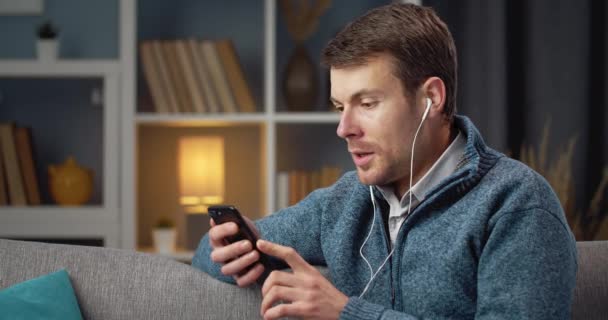 Handsome man in earphones having video chat on smartphone — Stock video