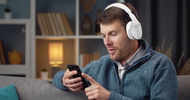 Relaxed man listening music in headphones on couch — Stockvideo