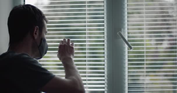 Man in protective mask looking through window blinds — Stock video