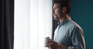 Handsome man with cup of coffee looking out of window