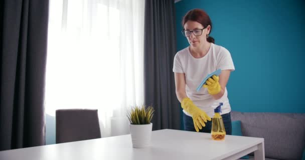 Mature woman in rubber gloves wiping white table at home