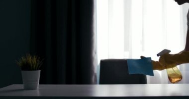 Side view of housewife in gloves wiping dust on table