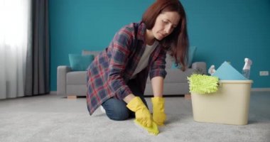 Woman in gloves standing on knees while cleaning carpet