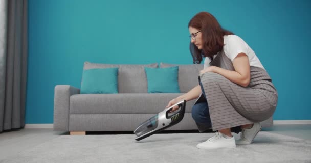 Mature woman in apron cleaning carpet with vacuum — 비디오