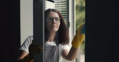 Olgun kadın pencereleri bez ve temizleyici spreyle temizliyor.