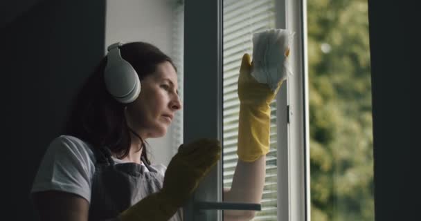 Ama de casa en auriculares lavando ventanas en casa — Vídeos de Stock