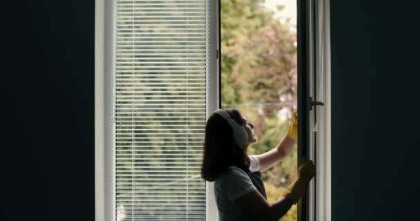 Gammal hemmafru i handskar och hörlurar tvätta fönster — Stockvideo