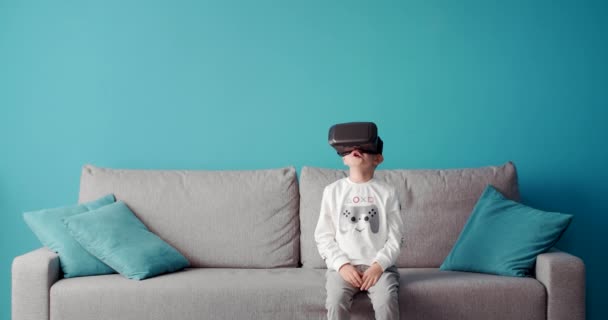 Happy little boy sitting on couch in virtual glasses — Stock Video