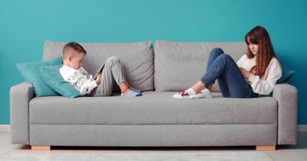 Sorella con fratello rilassante sul divano con gadget digitali — Video Stock