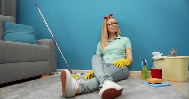 Домохозяйка в резиновых перчатках отдыхает на полу после уборки — стоковое видео