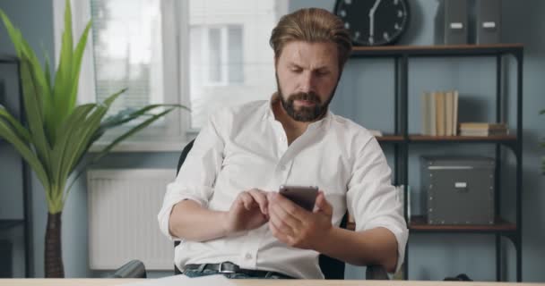 Homem confiante sentado no escritório moderno e usando smartphone — Vídeo de Stock
