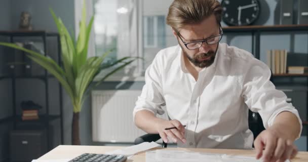 Homme barbu à l'aide d'une calculatrice pour vérifier les factures au bureau — Video