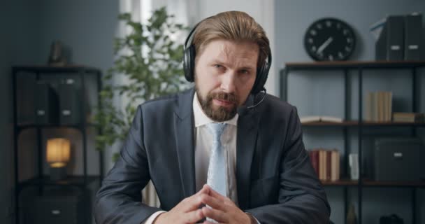 Biznesmen w słuchawkach nasłuchiwanie partnerów podczas rozmowy wideo — Wideo stockowe
