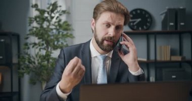 Resmi takım elbiseli meşgul bir adam oturmuş akıllı telefondan konuşuyor.