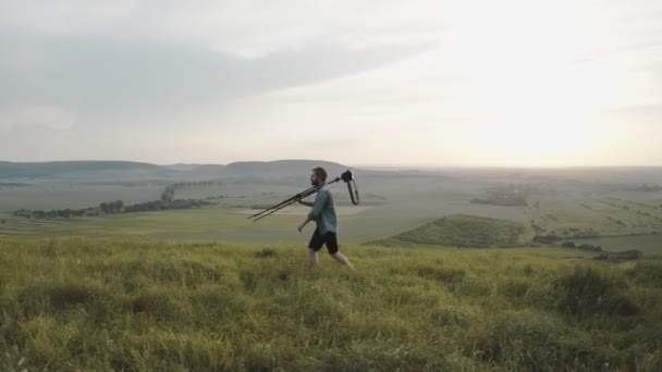 Vousatý muž kráčející po kopci se stativem a digitálním fotoaparátem — Stock video